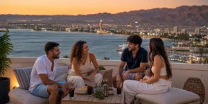 ארבעה חברים צעירים במרפסת דירת נופש מול מפרץ אילת בשעת השקיעה