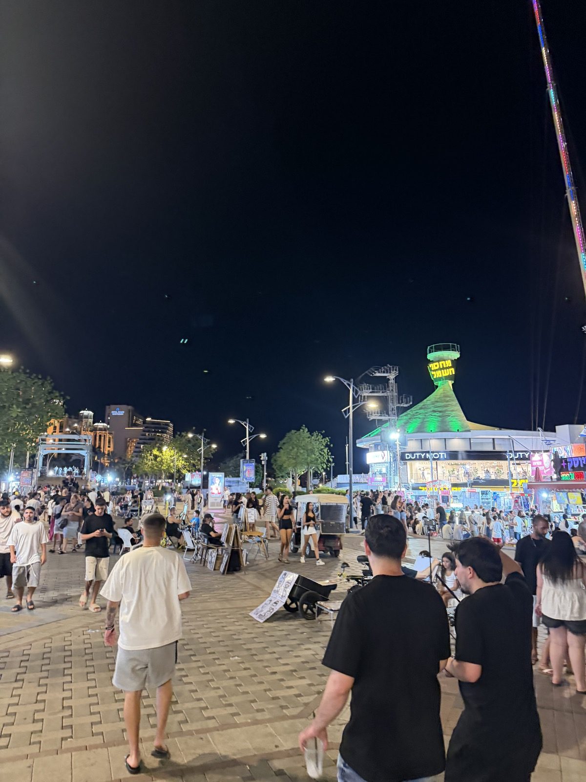 מטיילים ודוכנים מוארים בטיילת אילת בשעות הלילה