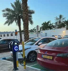 רכב חשמלי מחובר לעמדת גרינספוט ברחוב תרשיש באילת, לצד דקלים
